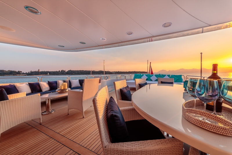 €200K Yacht Charter inclusions, luxury yacht deck seating area at sunset.